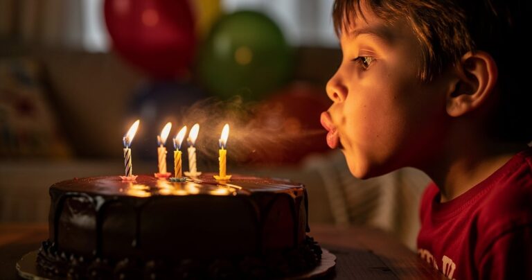 Enfant qui souffle les bougies de son gâteau d'anniversaire, lumière chaude des flammes